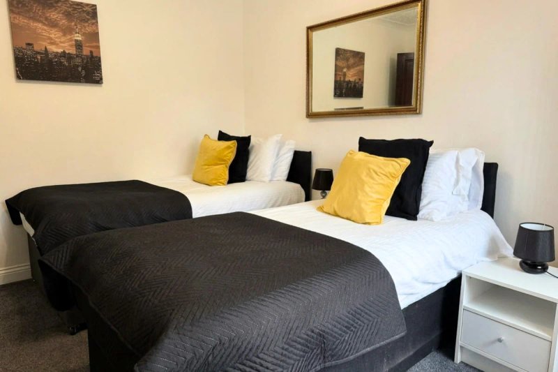 Modern bedroom with two single beds, black and white bedding, yellow accent pillows, nightstand and framed wall art