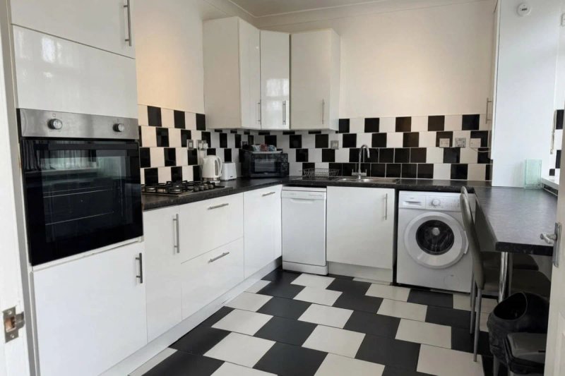 Modern kitchen with white cabinetry, black and white tile backsplash, built-in oven and washing machine