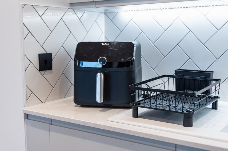 Modern kitchen countertop with black air fryer, white herringbone tile backsplash and black drying rack