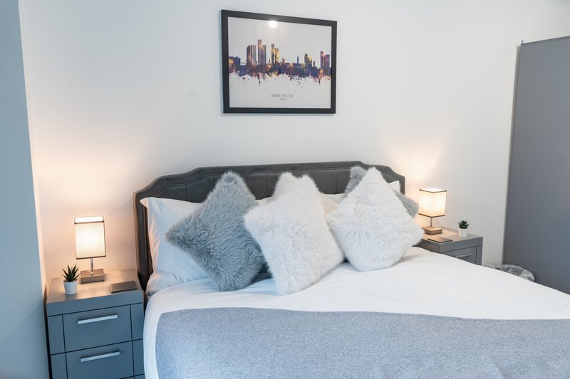 Modern bedroom with double bed, grey headboard, blue cushions and white bedside lamps