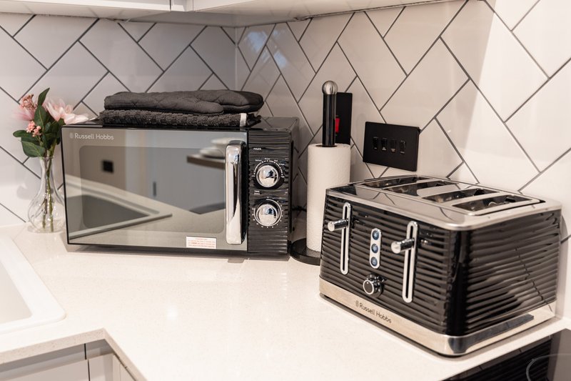 Kitchen counter with microwave, toaster, kettle and decorative items against herringbone tile backsplash