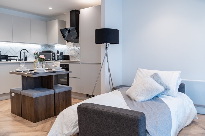 Open-plan studio with kitchen, dining island, bed with blue cushions and floor lamp