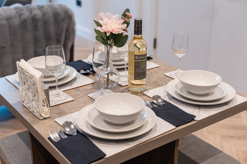 Dining table set for four with white dinnerware, wine bottle, pink flower arrangement and glasses