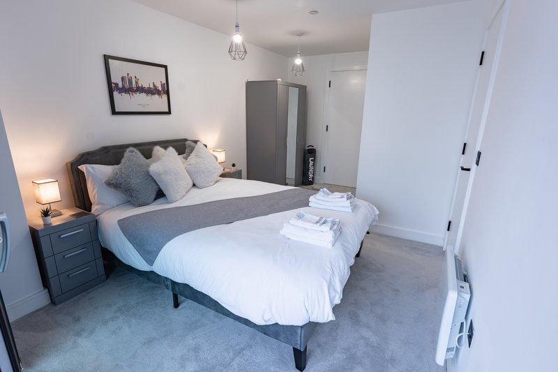 Modern bedroom with double bed, blue cushions, bedside lamps, and grey carpet flooring
