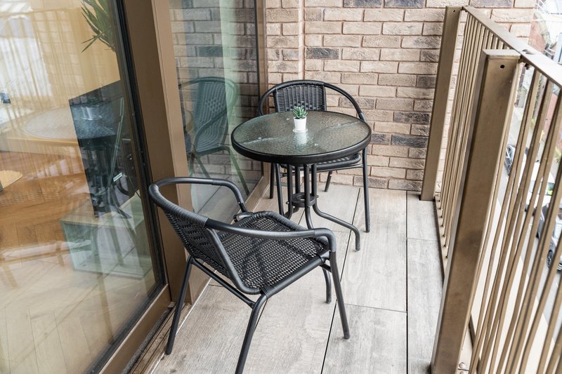 Small balcony with round table, two black metal chairs, brick wall and railing