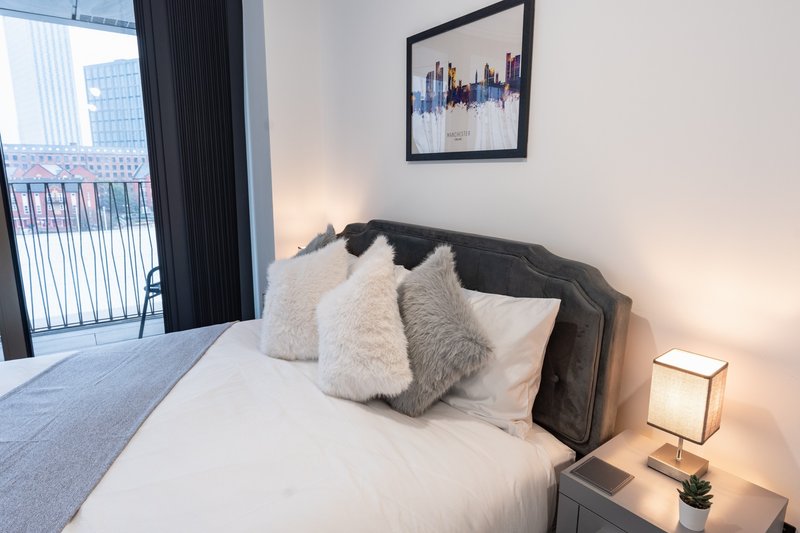 Modern bedroom with double bed, decorative pillows, bedside lamp and city view from balcony