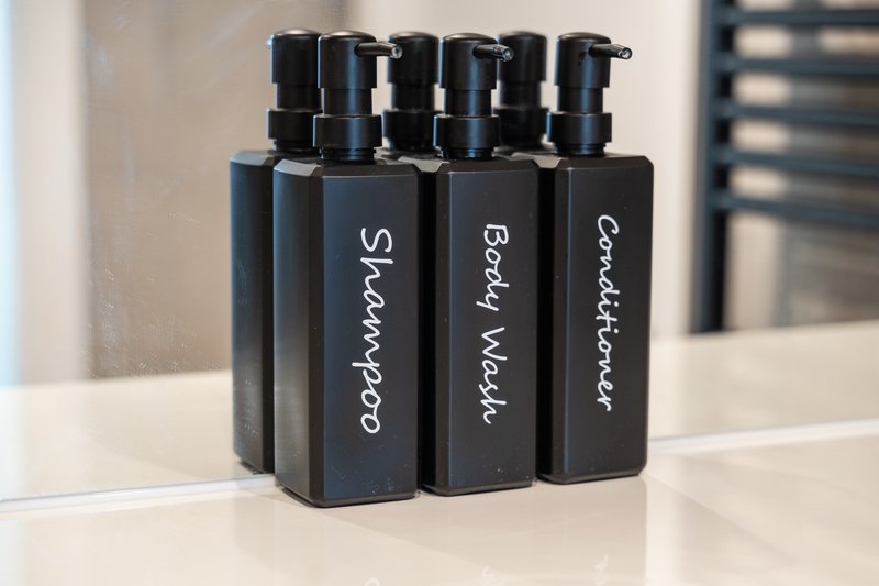 Three black pump bottles with handwritten labels on white bathroom counter