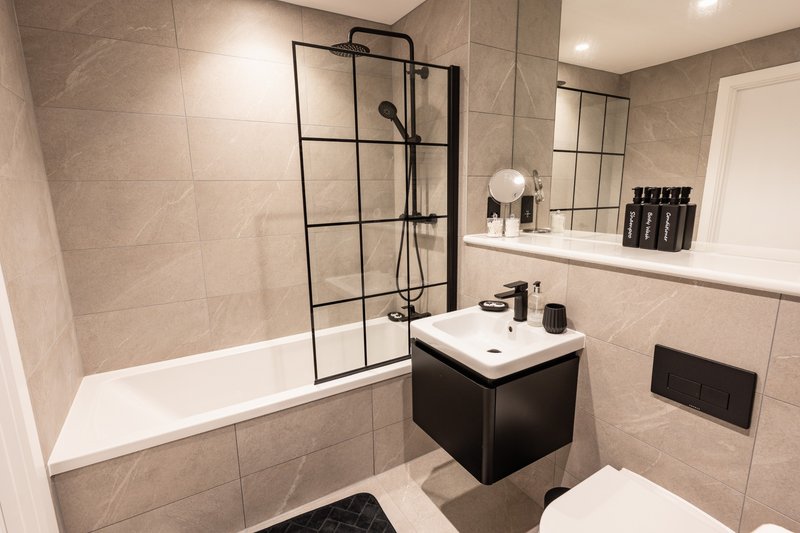 Modern bathroom with bathtub, black framed shower screen, vanity sink and toilet