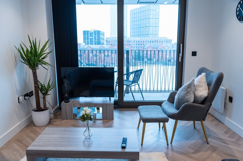 Modern living room with TV, comfortable armchair, potted plants, and city views from balcony