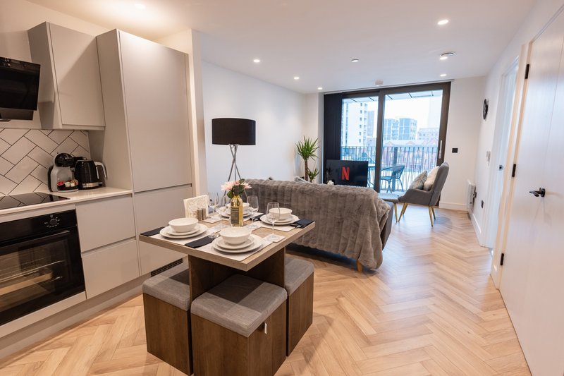 Modern open-plan kitchen and living area with dining table, sofa, and city views through large windows