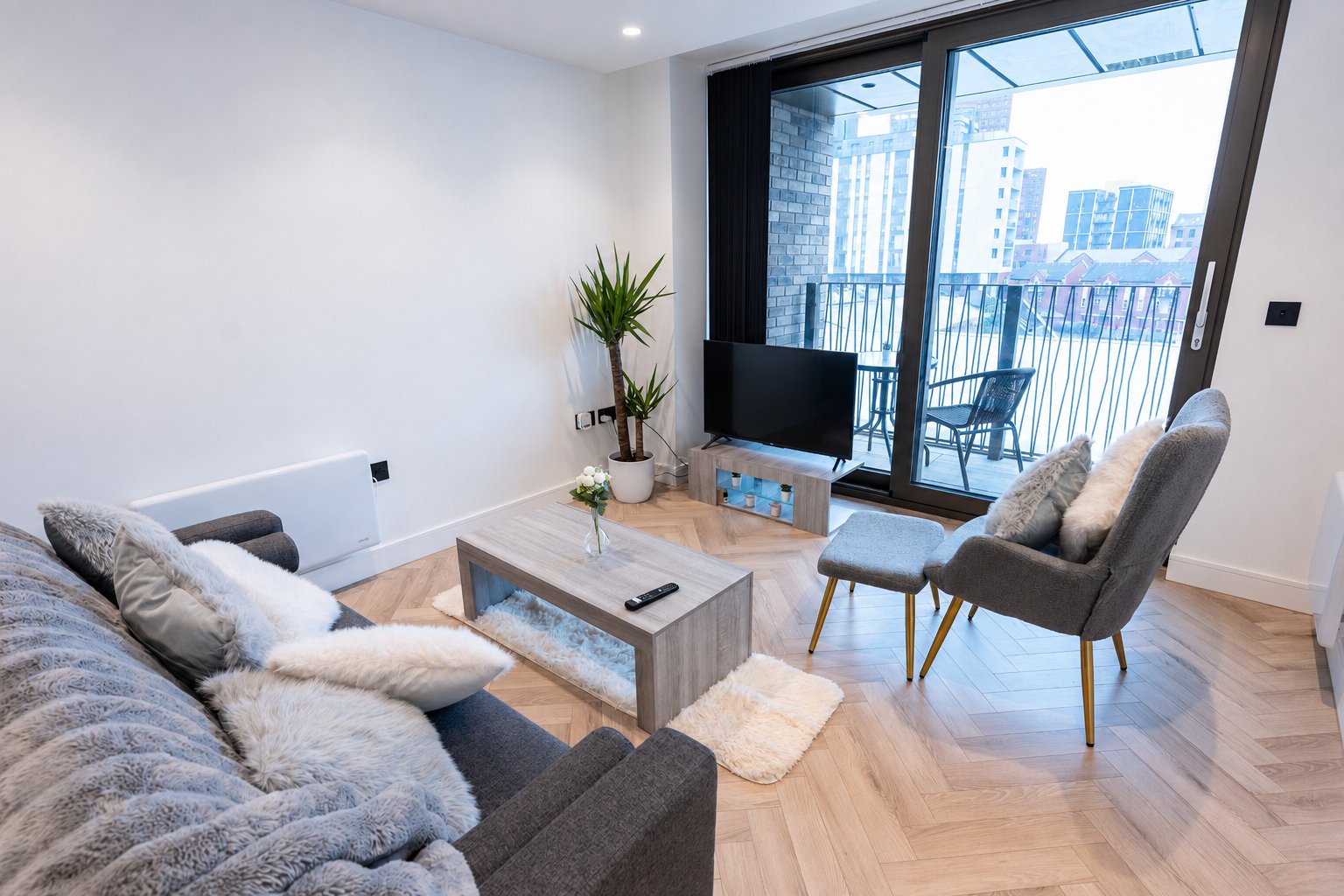 Modern living room with sofa, armchair, coffee table, and city views from balcony