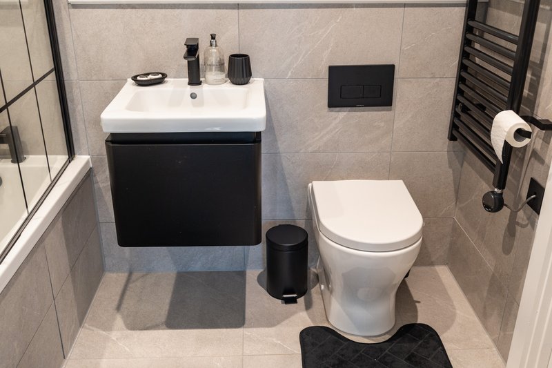 Modern bathroom with black vanity unit, white toilet, sink, and tiled walls