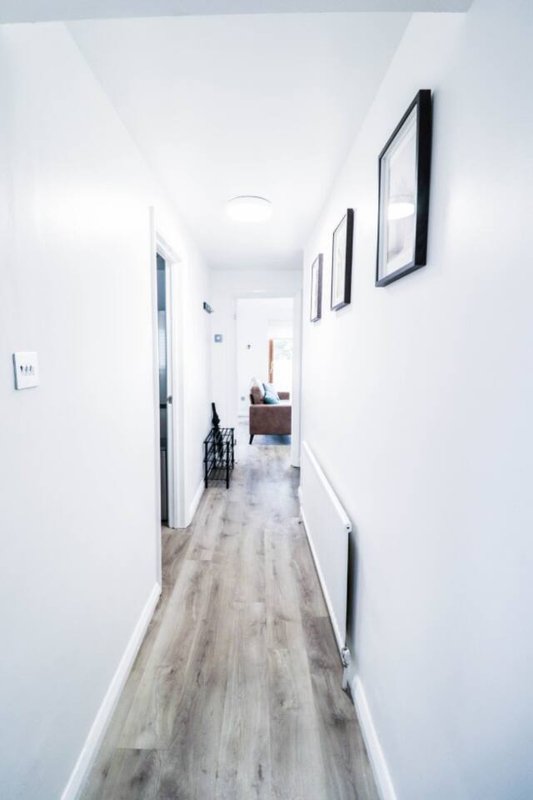 Long narrow hallway with white walls, framed artwork, light wood-effect flooring
