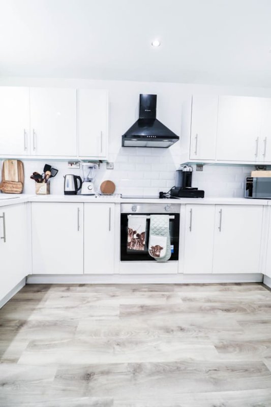 Modern white kitchen with black range hood, wooden flooring and countertop appliances