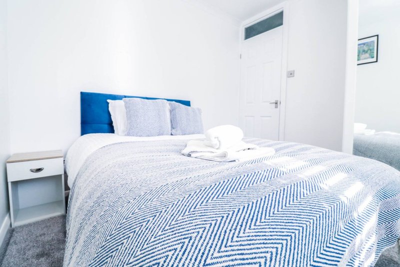Modern bedroom with double bed, blue headboard, white bedding and bedside table