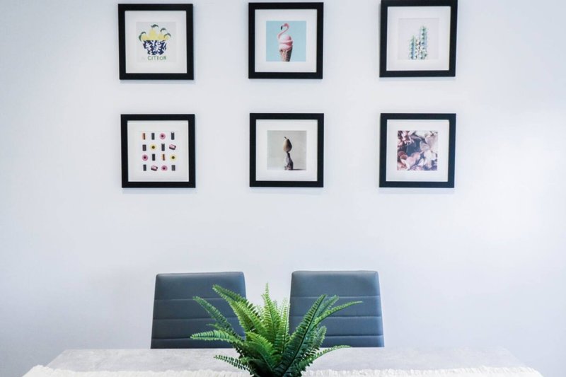 Modern dining area with white table, green plant, and six framed artworks on wall