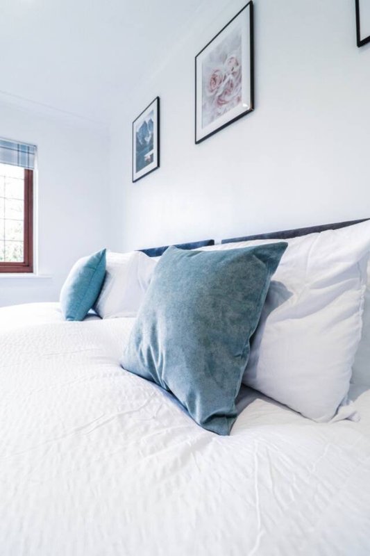 Bright bedroom with white bed, blue cushions, framed wall art and window
