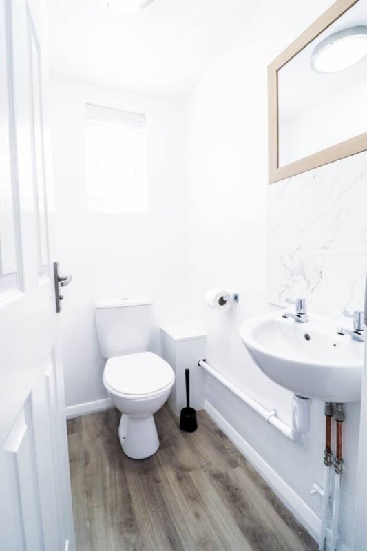 Clean modern bathroom with white toilet, pedestal sink, mirror and wooden floor