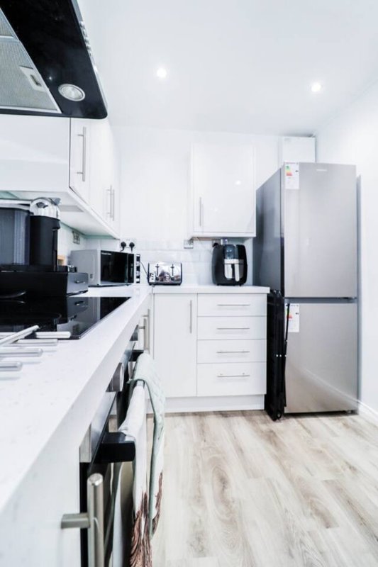 Modern white kitchen with stainless steel appliances, black stovetop, and wooden flooring