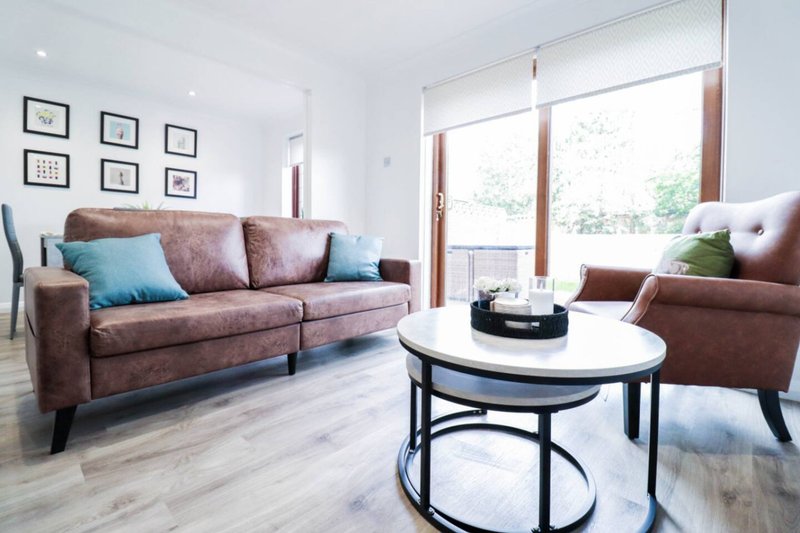 Modern living room with mauve sofa, armchair, oval coffee table and glass doors to garden