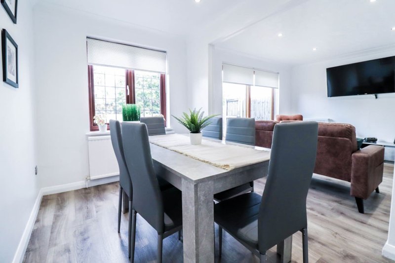 Modern open-plan living and dining area with marble table, grey chairs, sofa, and wall-mounted TV