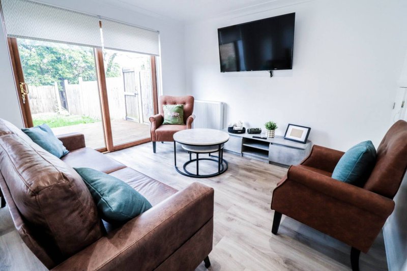 Bright living room with brown leather sofas, white round table, wall-mounted TV and patio doors