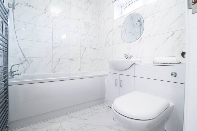 Modern bathroom with white marble tiles, toilet, sink, and bathtub with shower
