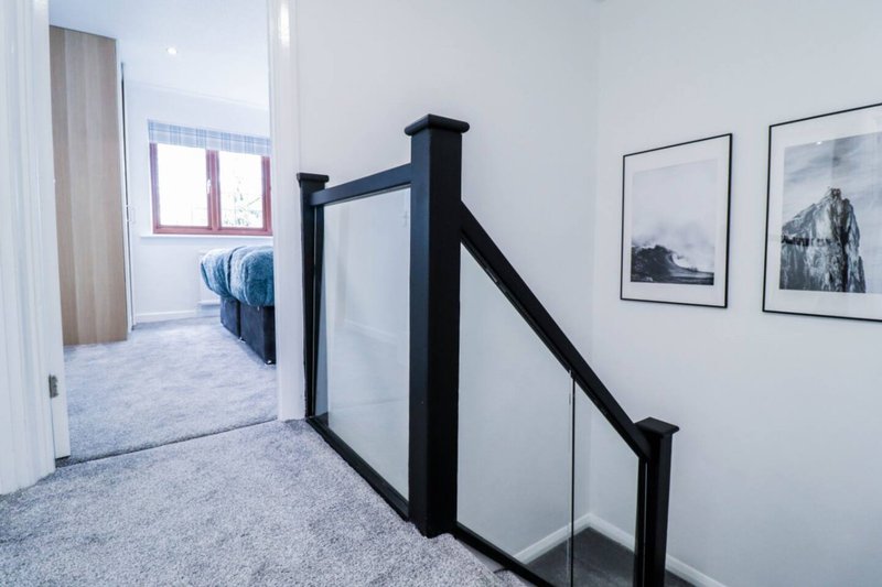Modern staircase landing with glass balustrade, grey carpet, framed landscape photos on white walls