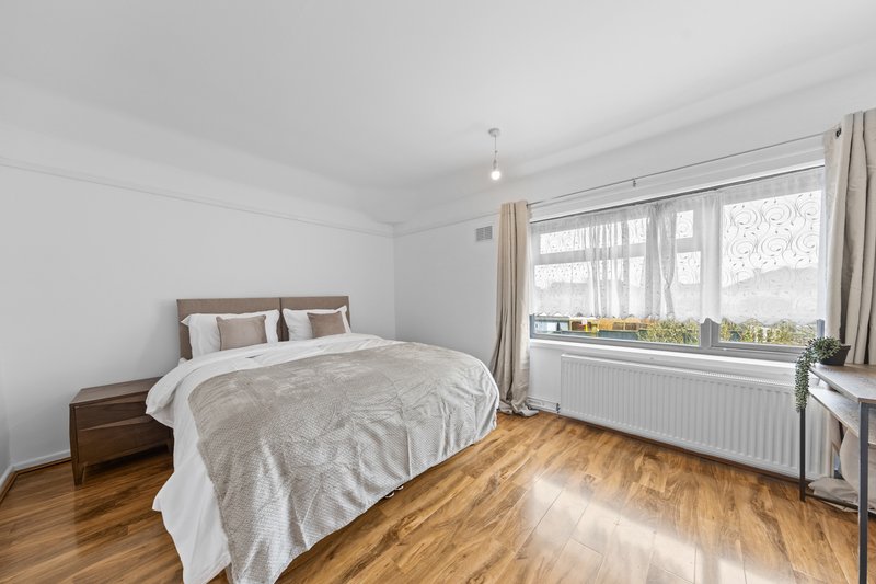 Bright bedroom with double bed, wooden floor, large windows and cream curtains