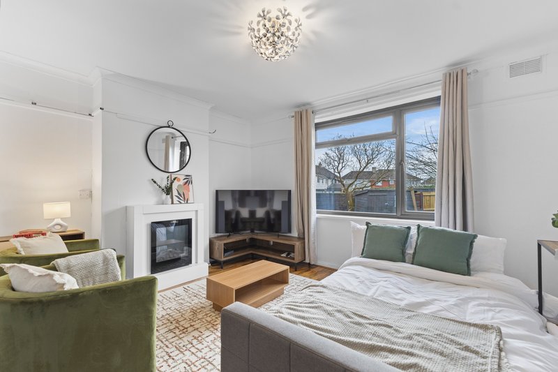 Bright modern bedroom with double bed, fireplace, green armchair and large windows overlooking garden