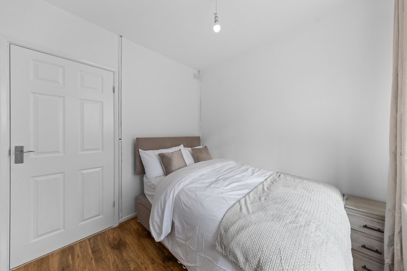 Bedroom with single bed, white bedding, wooden floor and white door