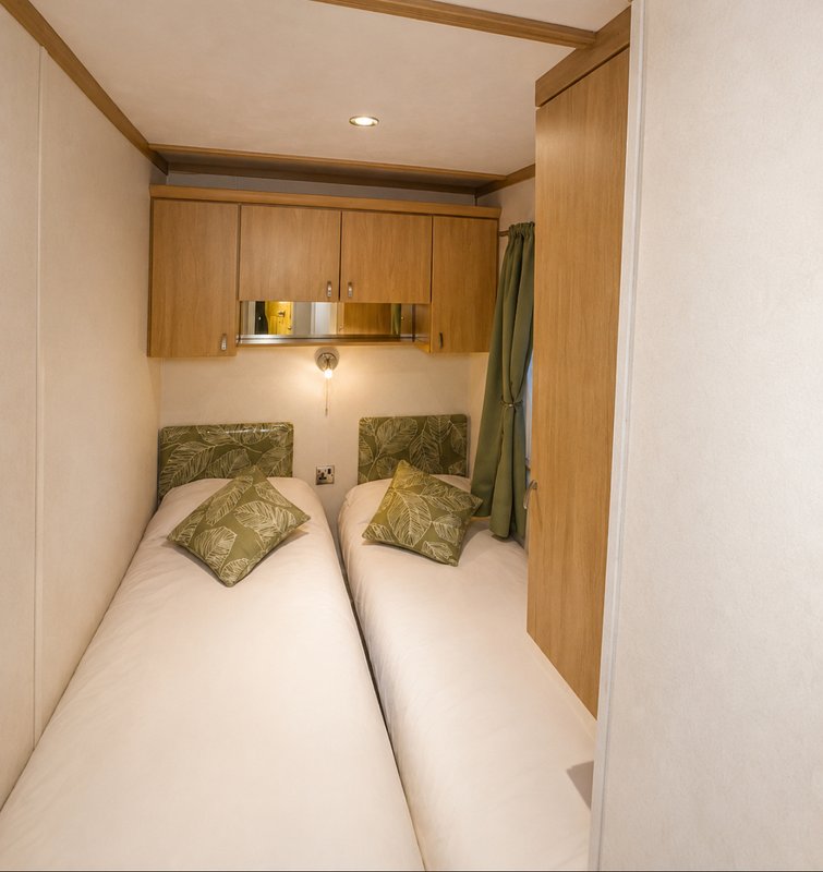 Narrow bedroom with two single beds, green cushions, wooden storage and recessed lighting