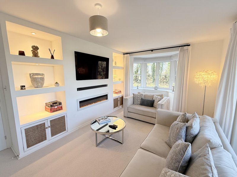 Modern living room with cream sofa, built-in shelving, fireplace, TV, and large window