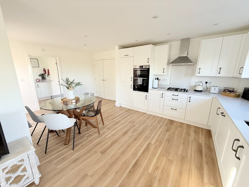 Open-plan kitchen and dining area with white cabinetry, wooden flooring and dining table