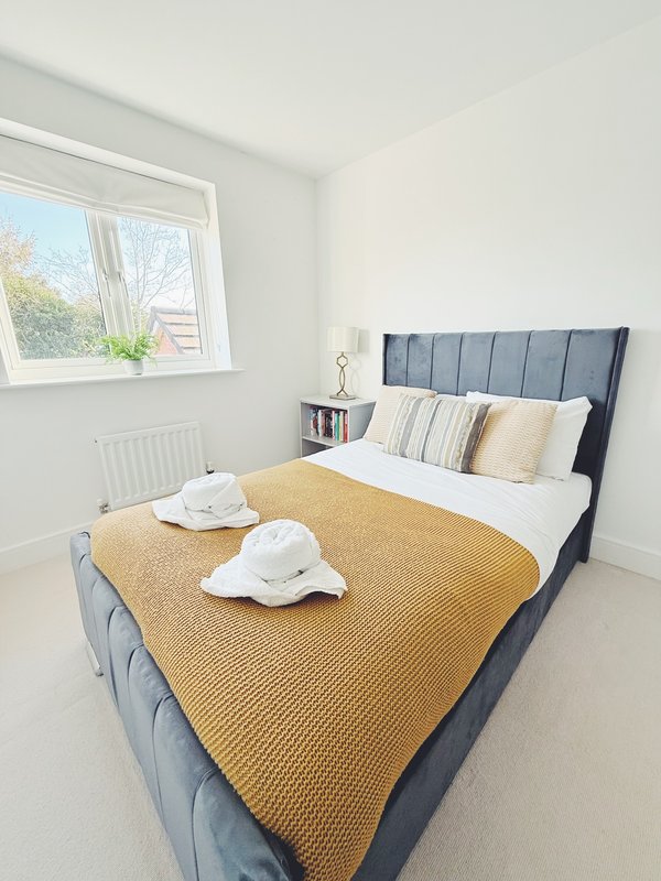 Bright bedroom with double bed, mustard throw, striped pillows and window view