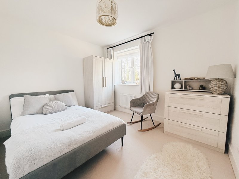 Bright modern bedroom with double bed, cream wardrobe, dresser, rocking chair and pendant light