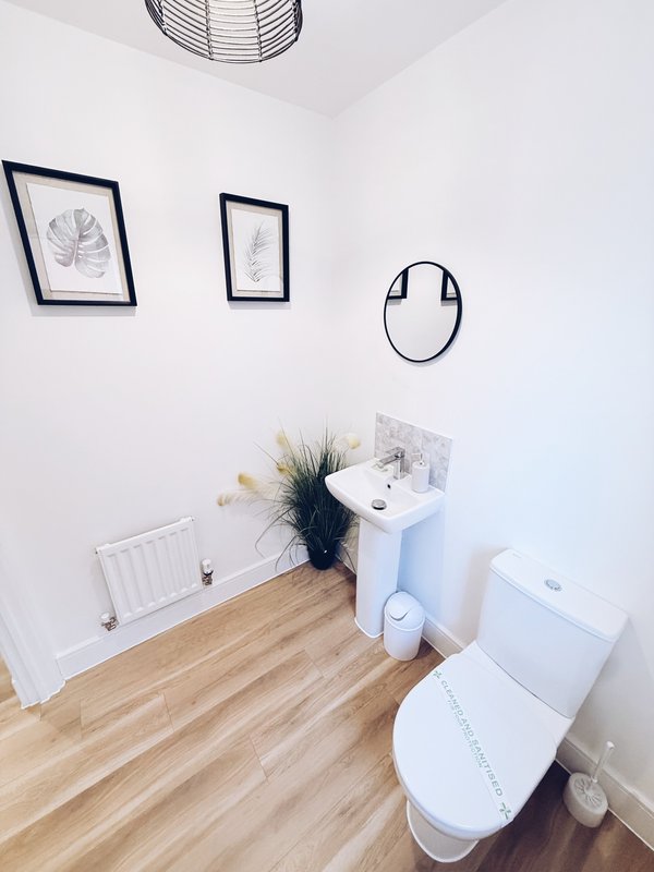 Modern bathroom with white toilet, sink, wooden floor, framed wall art and decorative items