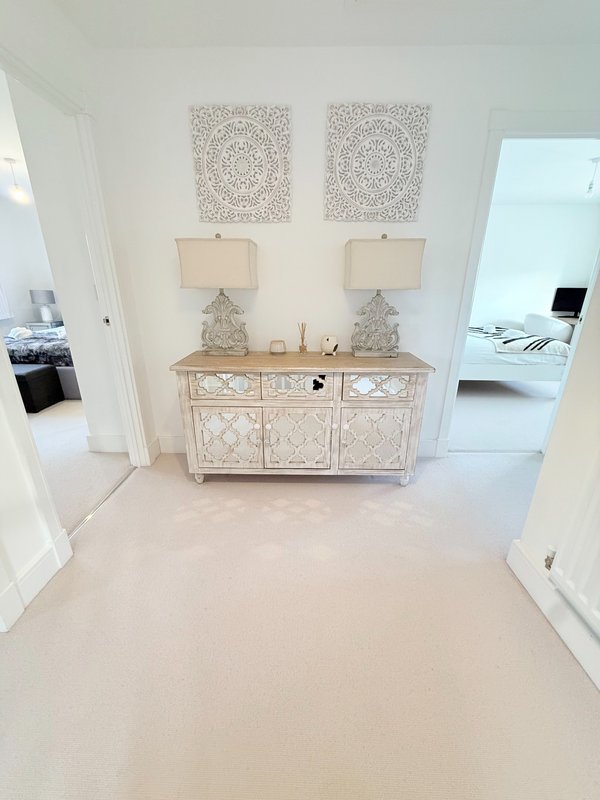 Bright hallway with decorative cabinet, table lamps, and framed wall art