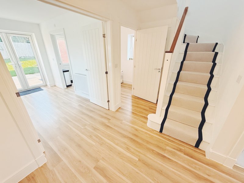 Bright hallway with wooden flooring, white doors, and staircase with black railings