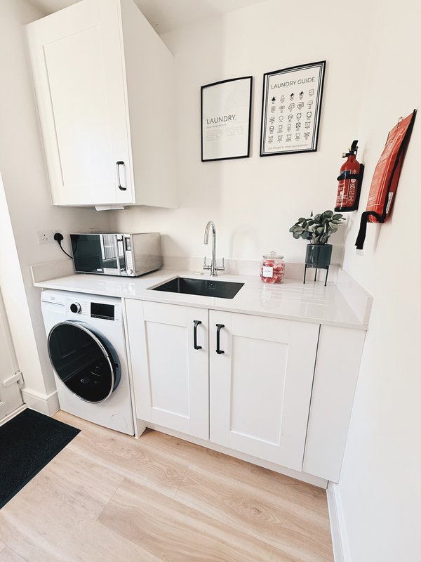 Modern white kitchenette with washing machine, sink, and wall-mounted storage cabinets