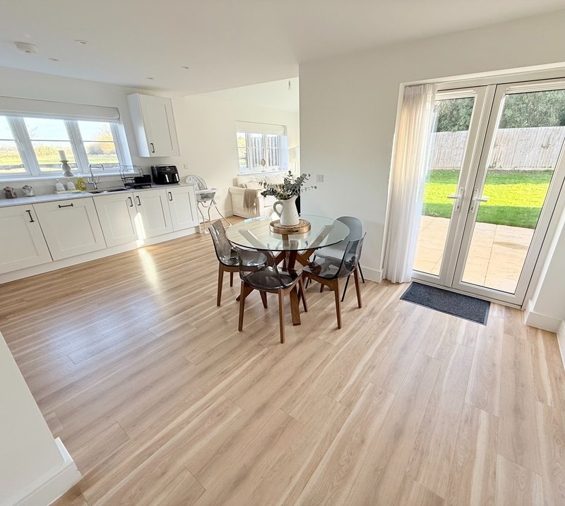 Open-plan kitchen and dining area with wooden flooring, white cabinetry, dining table with chairs, and glass doors to garden