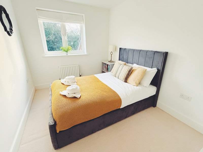 Bright bedroom with double bed, yellow throw, white pillows and natural light from window