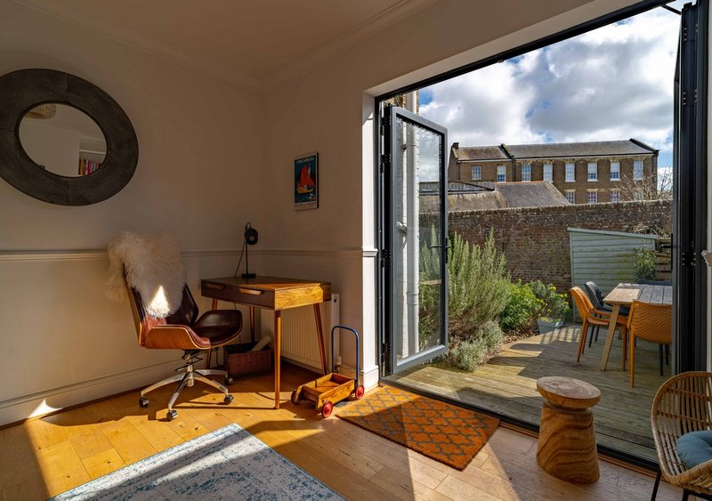 Bright office space with wooden desk, office chair, and open doors leading to garden terrace