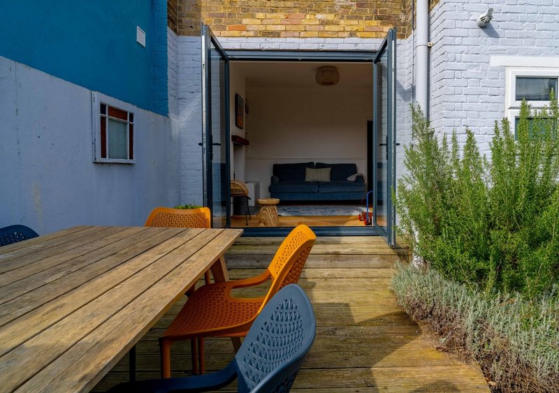 Outdoor patio with wooden table and chairs, open garden room door with sofa visible inside