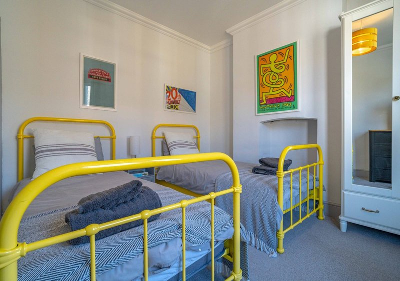 Bright bedroom with two yellow metal-frame beds, blue bedding, and colorful wall art