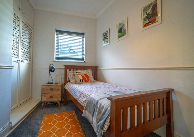 Bedroom with wooden single bed, bedside table, window with blinds and framed wall art