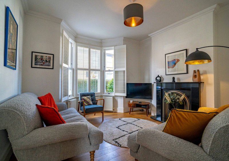 Bright living room with grey sofas, fireplace, bay windows, and modern lighting fixtures