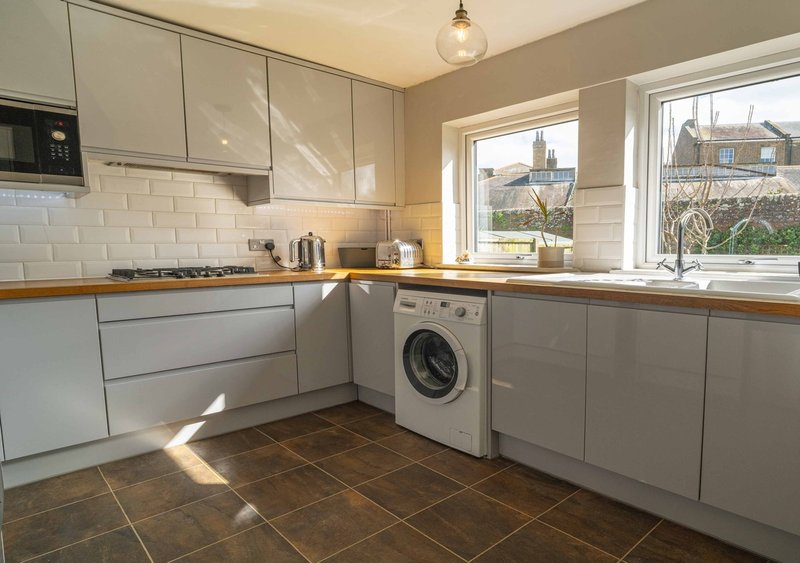 Modern kitchen with gray cabinetry, washing machine, and views through windows to garden
