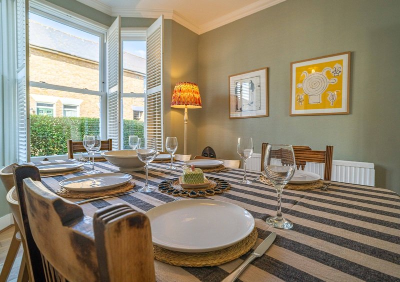 Dining room with set table, wooden chairs, striped runner, large windows and wall art
