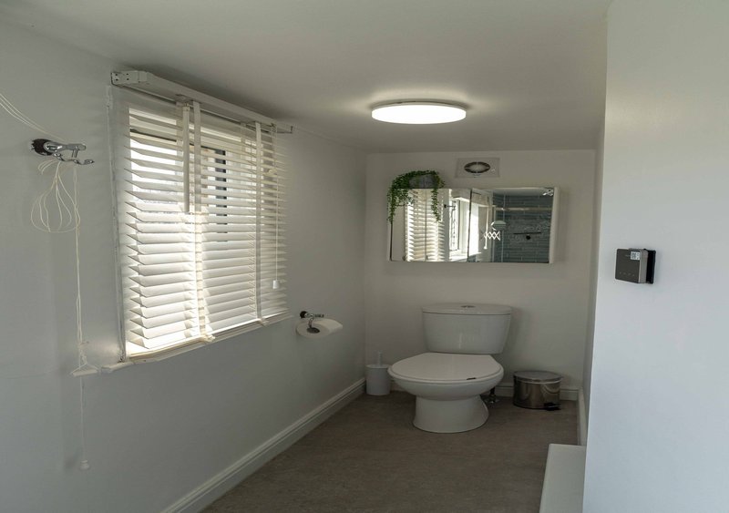 Modern bathroom with toilet, sink, mirror, window with shutters and recessed lighting
